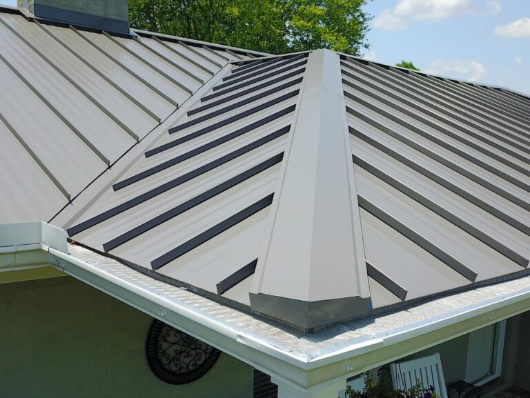 roof replacement cost raleigh nc Close-up of a modern gray metal roof with standing seam panels and a clean white gutter system under a sunny sky. Trees are visible in the background.