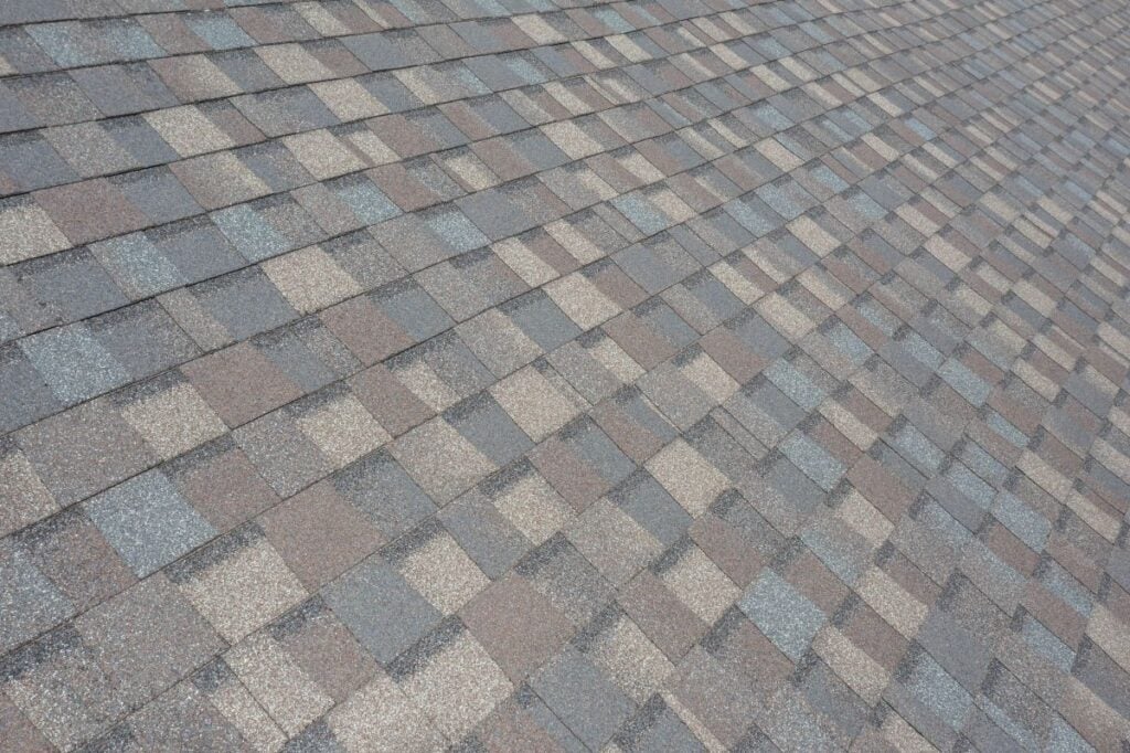 best roofing materials north carolina Close-up view of a roof covered with asphalt shingles in a pattern of gray and brown tones, arranged in overlapping rows.