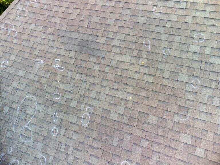 Gray shingle roof with multiple chalk circles marking hail damage spots, indicating areas for repair or inspection.