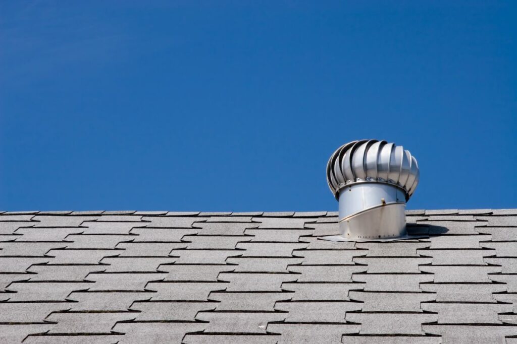 Gray shingled roof with a metal turbine vent against a clear blue sky.