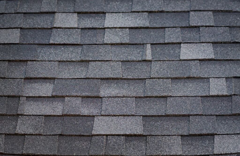 Close-up of gray asphalt roof shingles arranged in a regular overlapping pattern, showing texture and slight variations in color—a detail often highlighted by top roofing companies Concord NC trusts for quality workmanship.